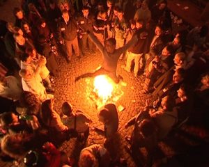 a man jumping over fire and surrounded people clapping